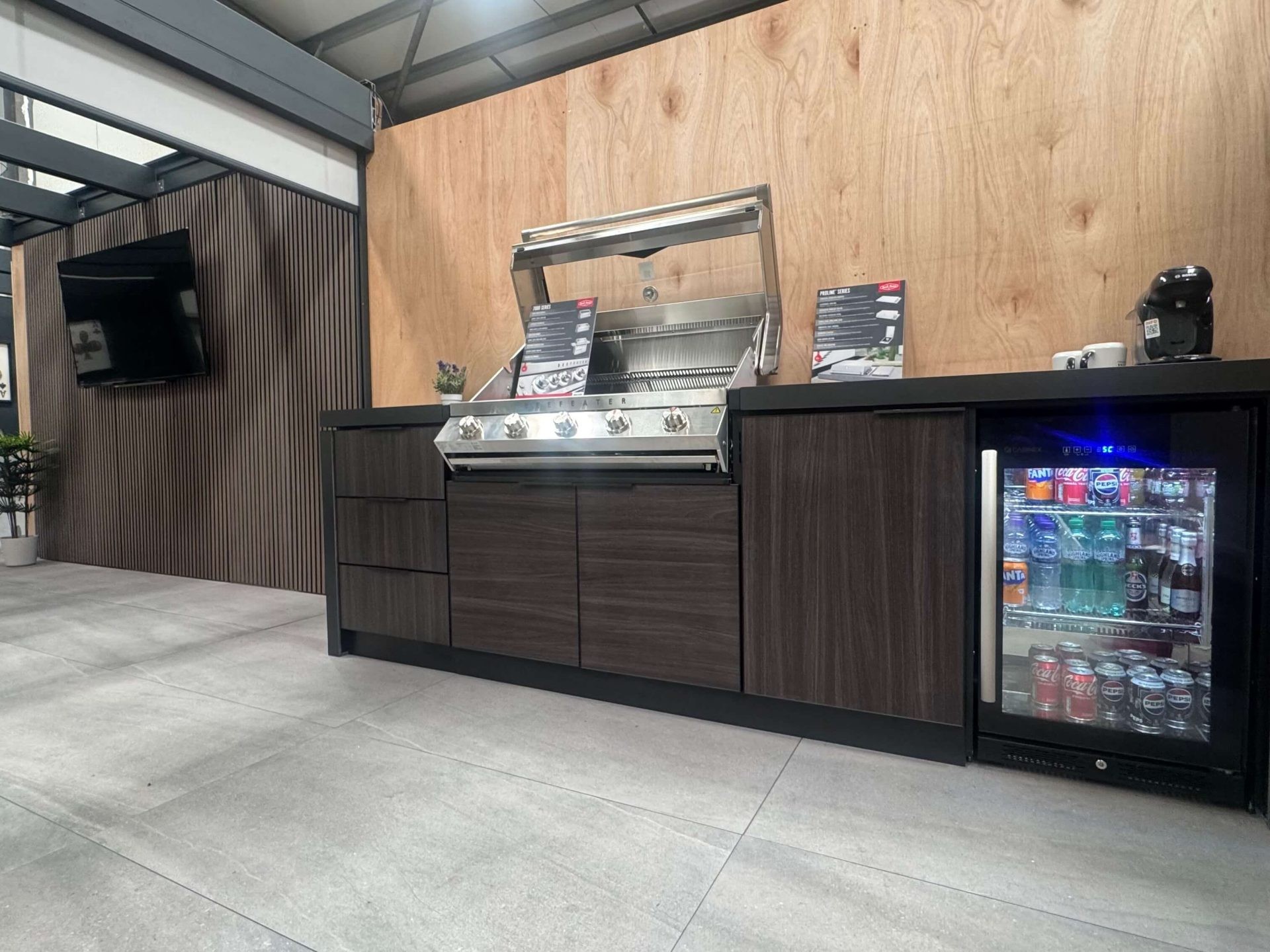 Stainless steel silver beef eater grill installed on a dark brown timber outdoor kitchen unit with a fridge