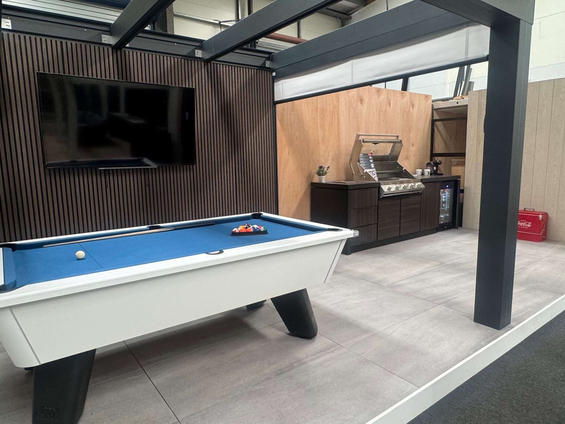 Grey design line veranda, furnished with a white pool table, black wall mounted tv and white pot plant