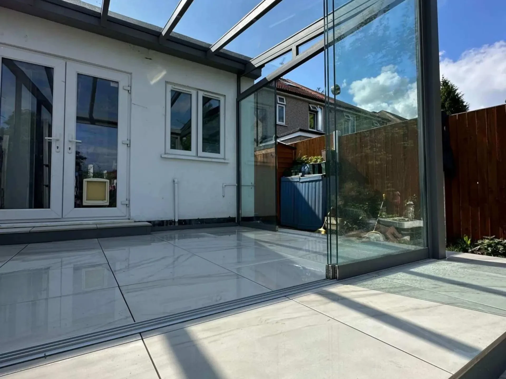 Anthracite grey aluminium frame glass room veranda with glass sliding doors, safety glass roof and LED spot lights, over a white porcelain patio