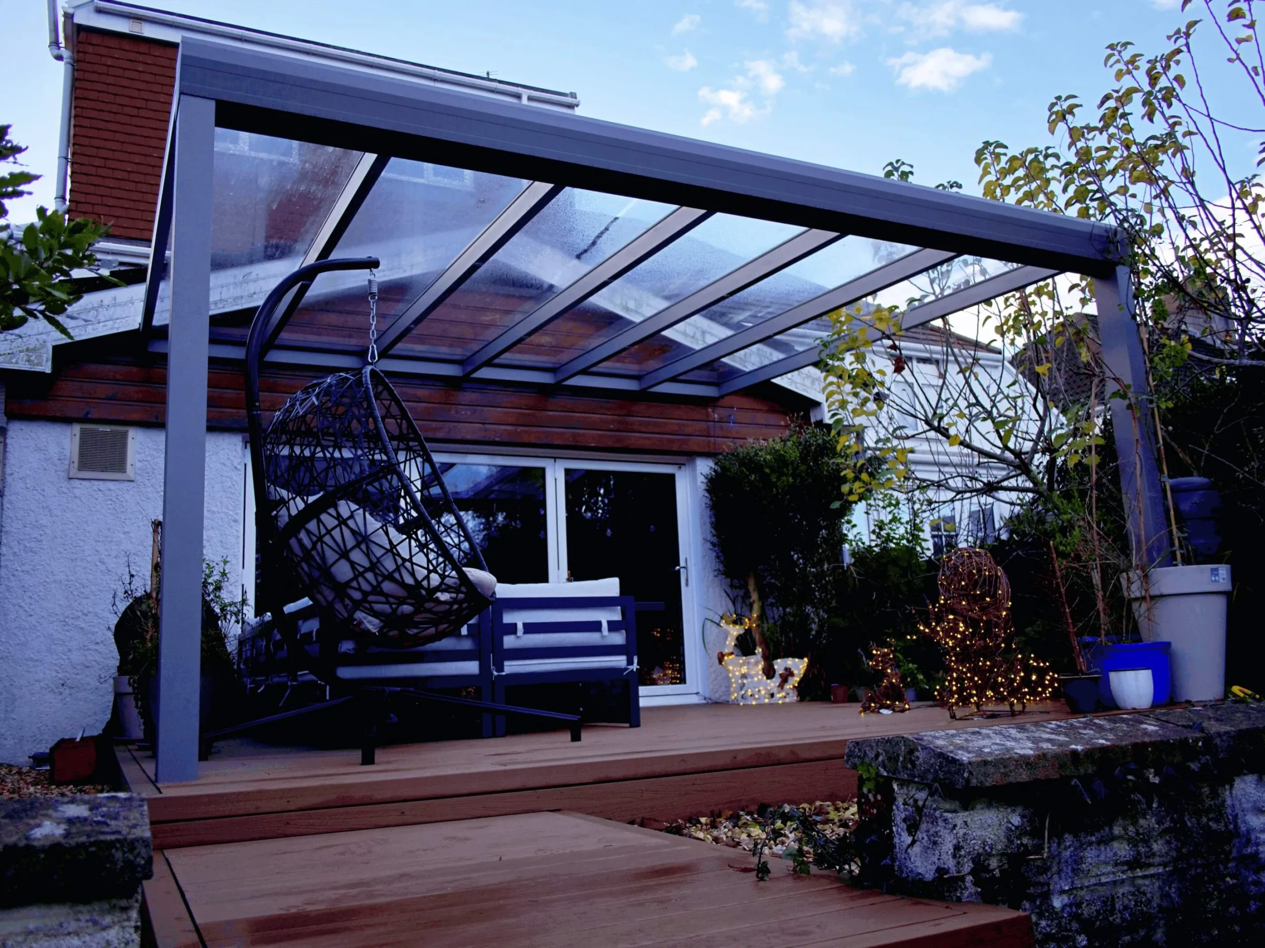 Anthracite grey glass roof veranda with a brown hammock chair and Christmas decor and lighting.
