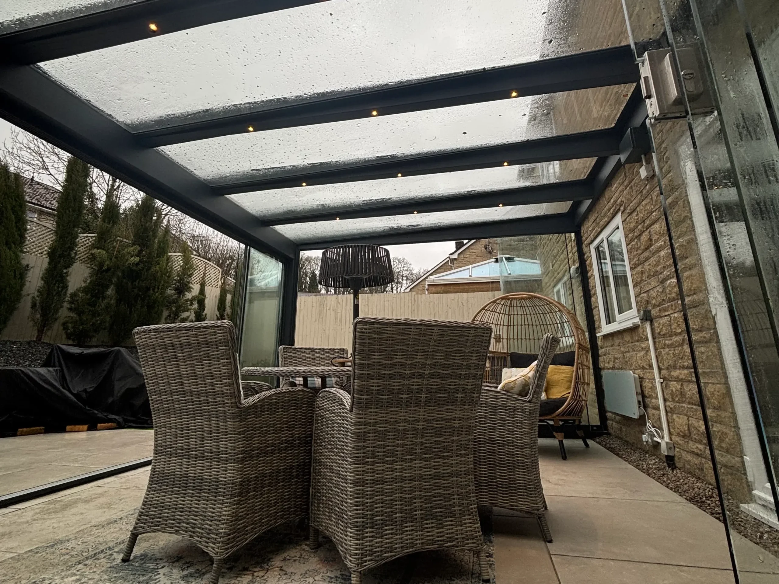 Interior of an anthracite grey aluminium framed glass room veranda with LED spot lights, furnished with a beige rattan garden dining set
