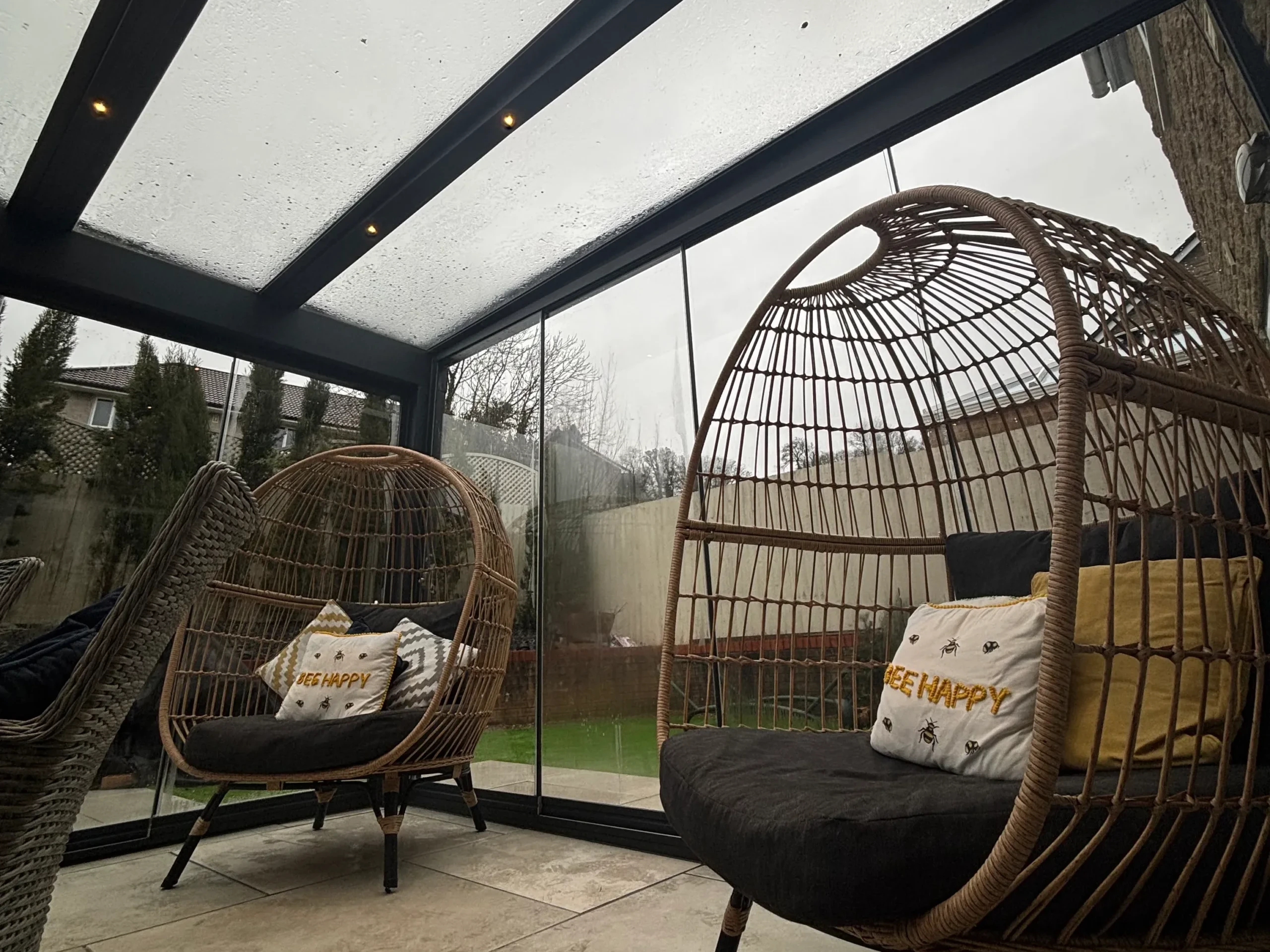 Two brown hammock chairs inside an anthracite grey aluminium framed glass room veranda with LED spot lights turned on.