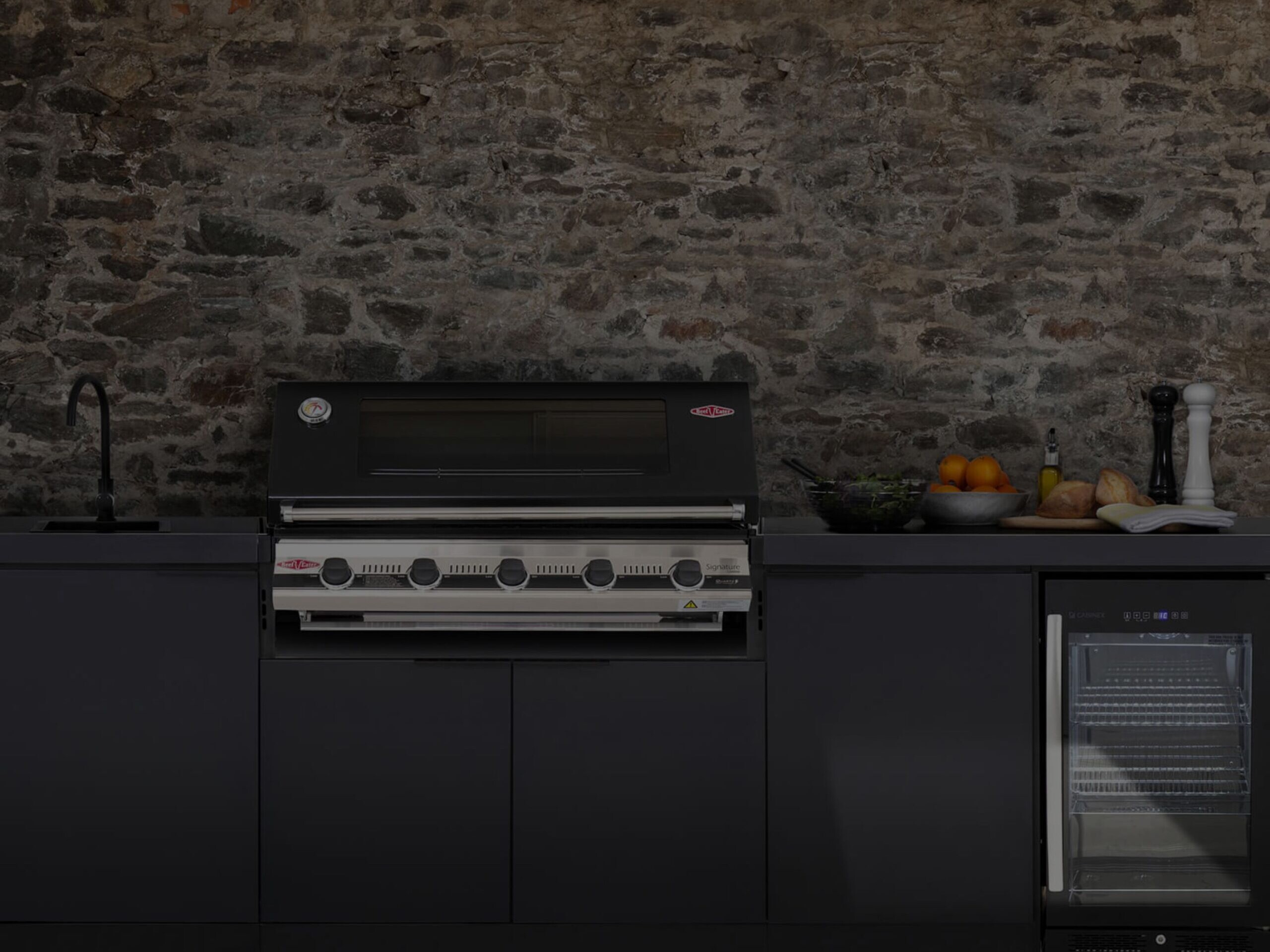 Black composite outdoor kitchen unit with a black and chrome grill, tap and fridge.