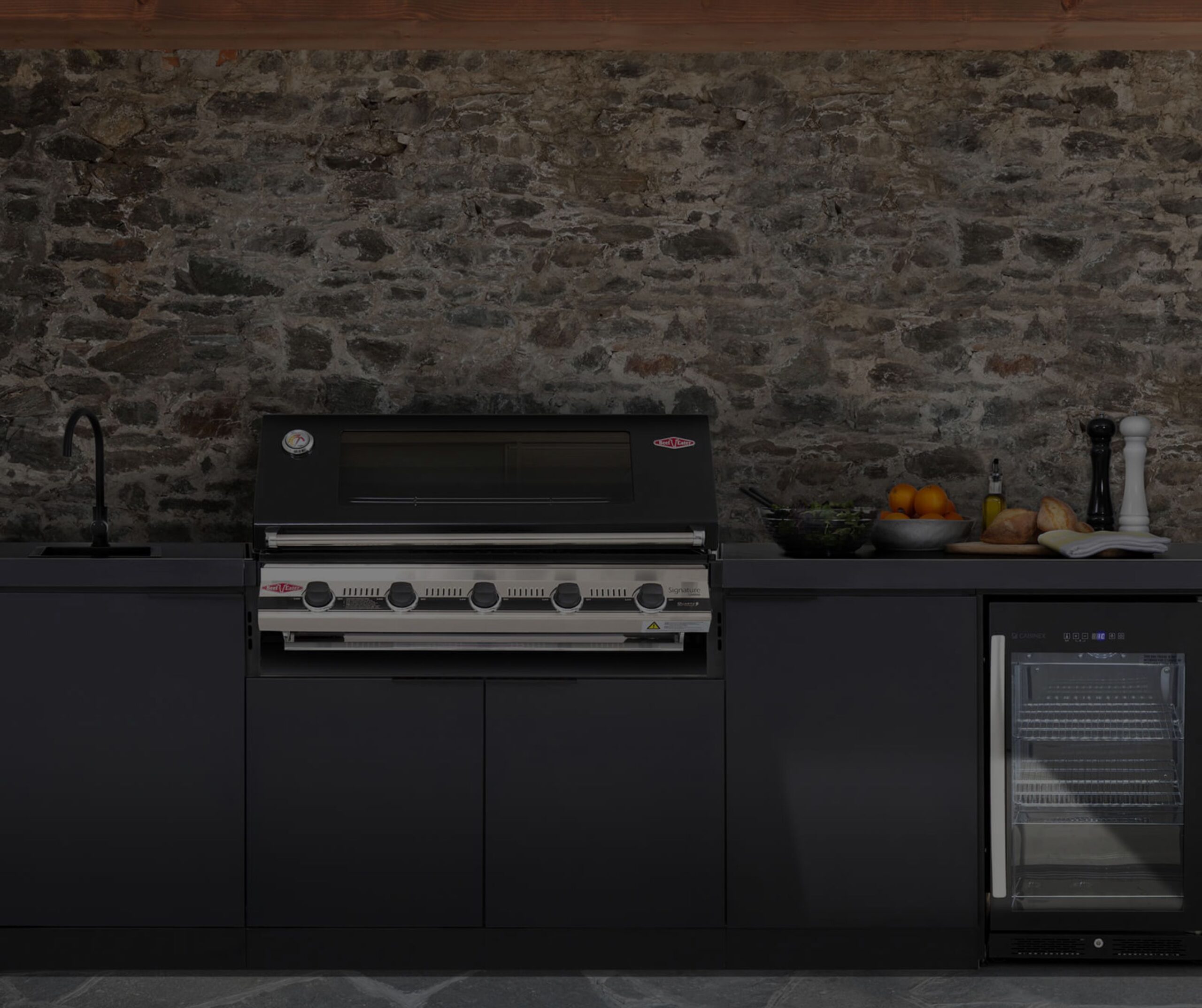 Black composite outdoor kitchen unit with a black and chrome grill, tap and fridge.