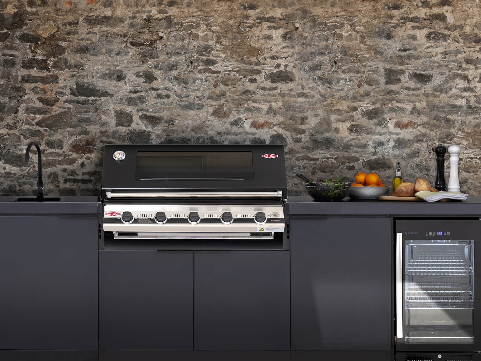 Black composite outdoor kitchen unit with a black and chrome grill, tap and fridge.