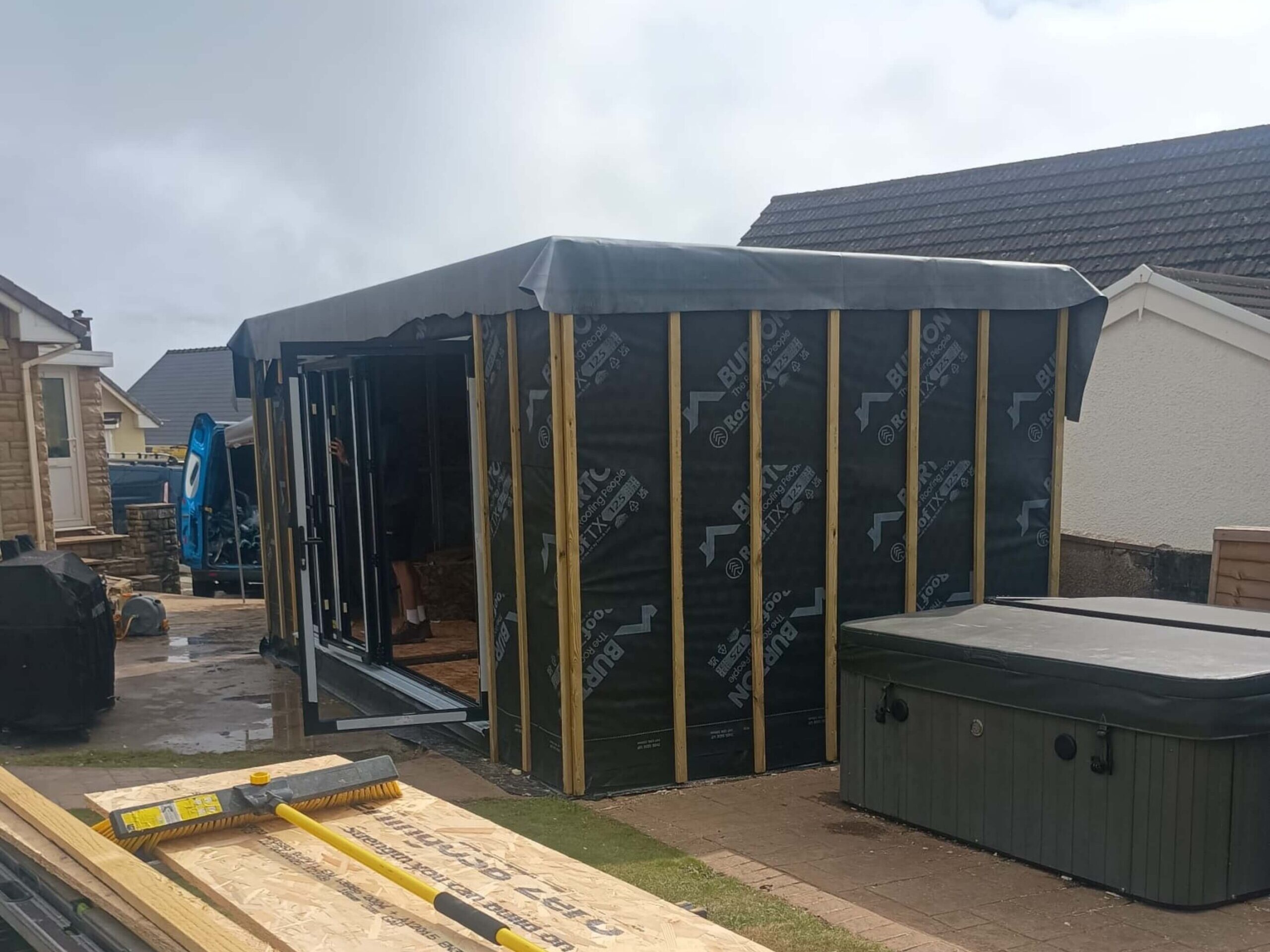 Unfinished grey composite cladded insulated garden room with black aluminium framed bifold doors and a black rubber roof.