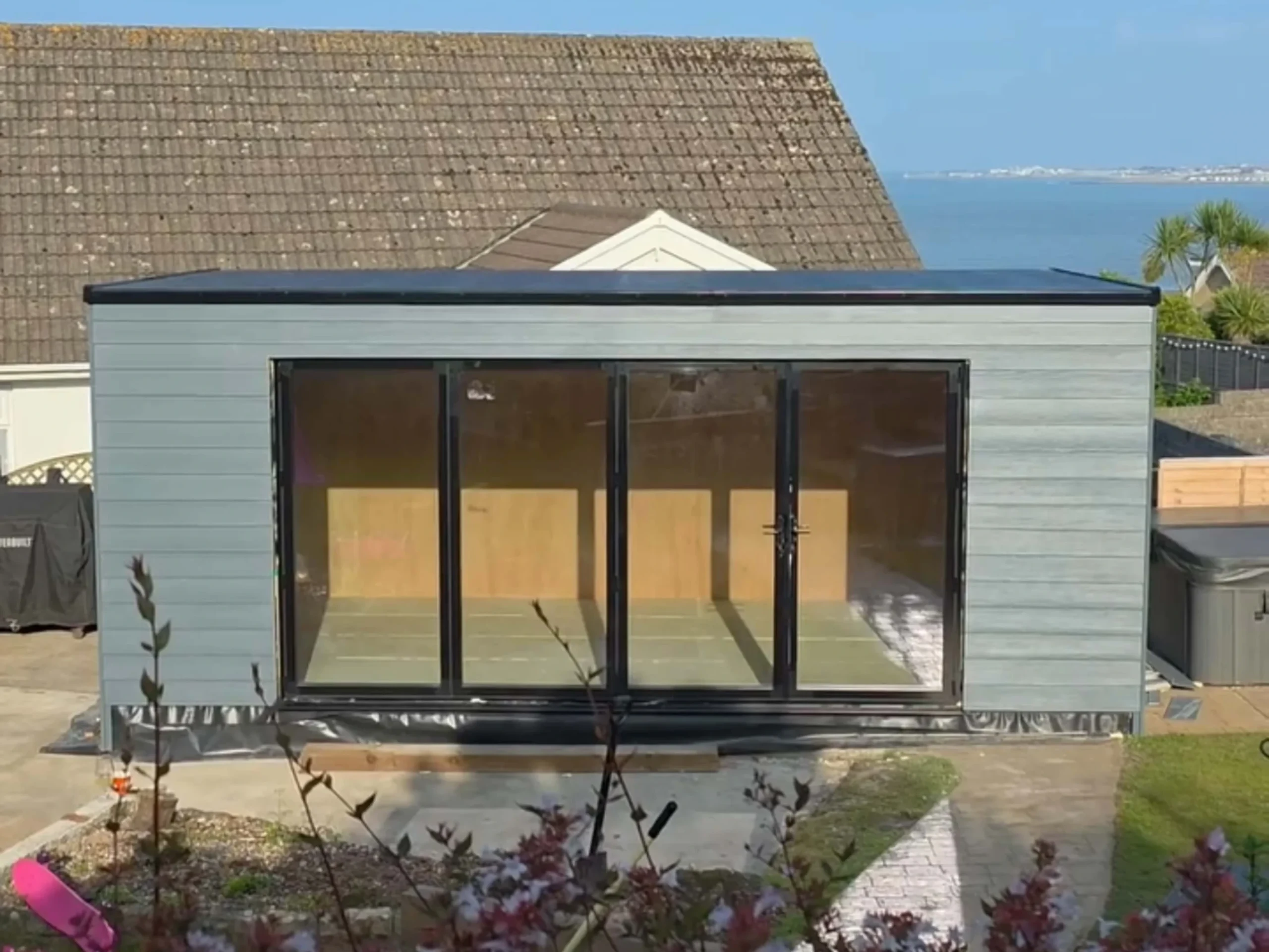 Grey composite cladded insulated garden room with black aluminium framed bifold doors and a black rubber roof.