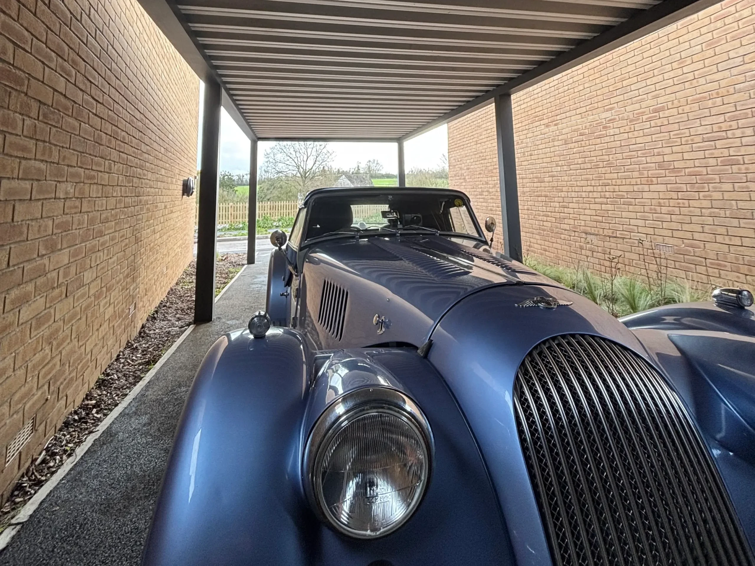Anthracite grey aluminium framed carport with a white box profile aluminium roof, standing on 4 posts and sheltering a metallic blue classic car.
