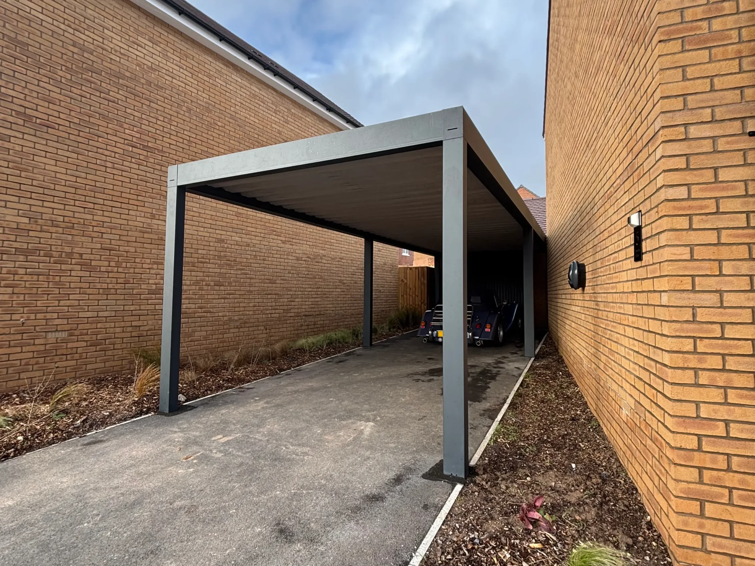 Anthracite grey aluminium framed carport with a box profile white aluminium roof, standing on 4 posts.