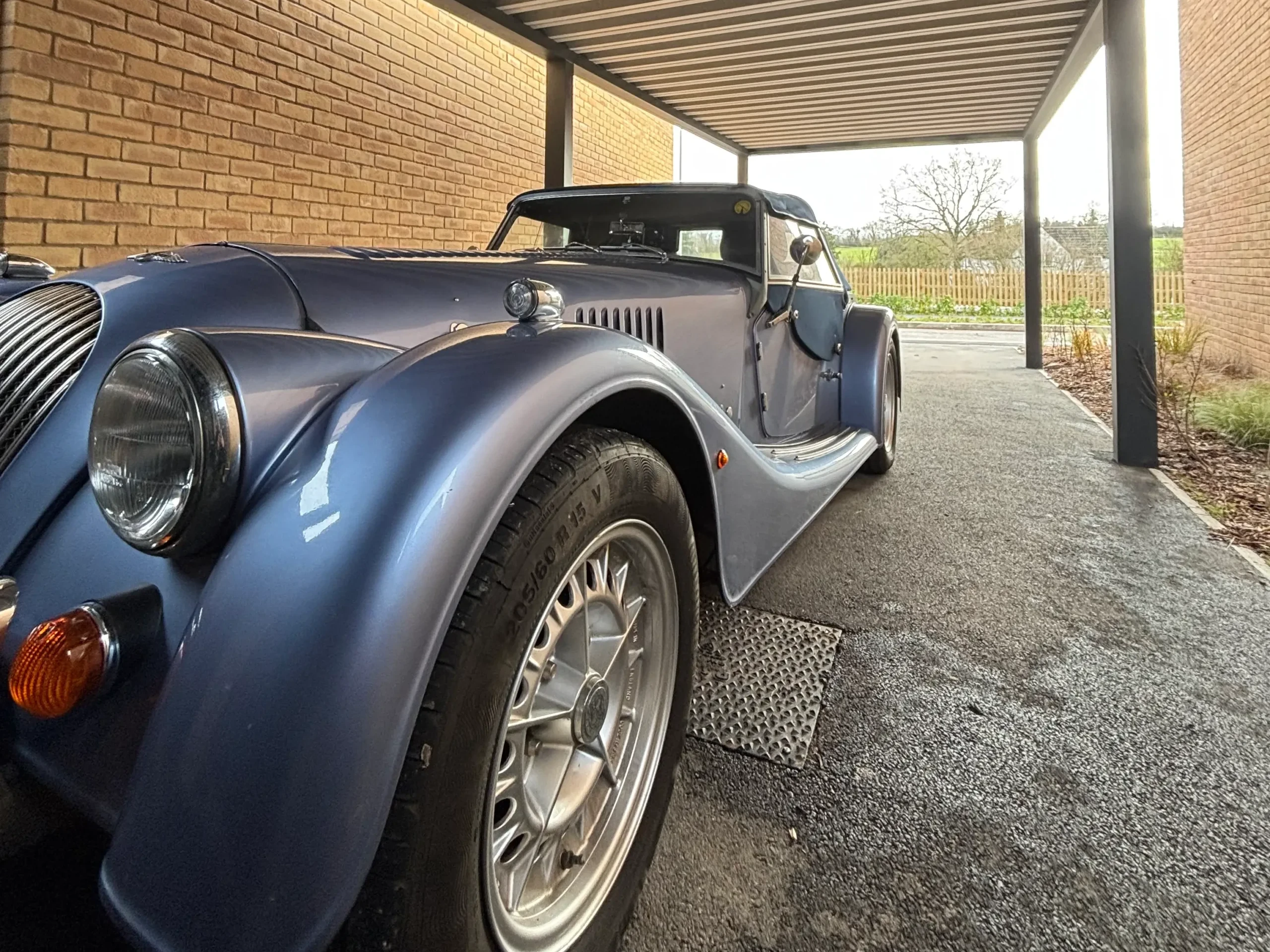 Anthracite grey aluminium framed carport with a white box profile aluminium roof, standing on 4 posts and sheltering a metallic blue classic car.