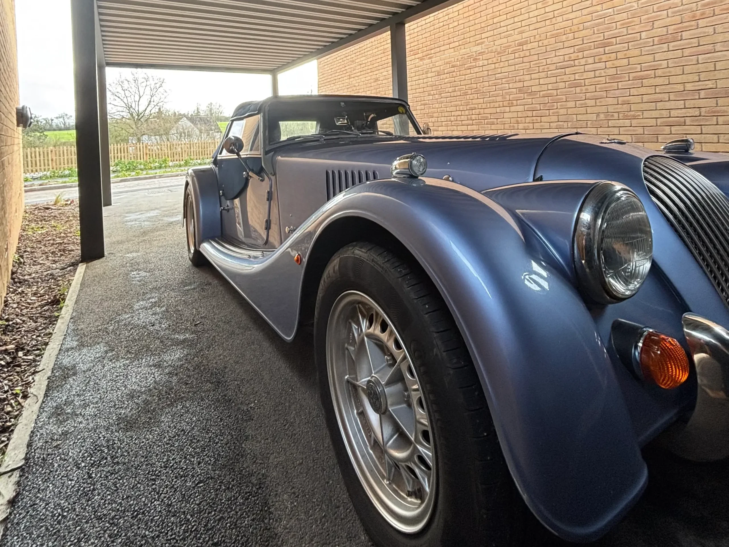 Anthracite grey aluminium framed carport with a white box profile aluminium roof, standing on 4 posts and sheltering a metallic blue classic car.