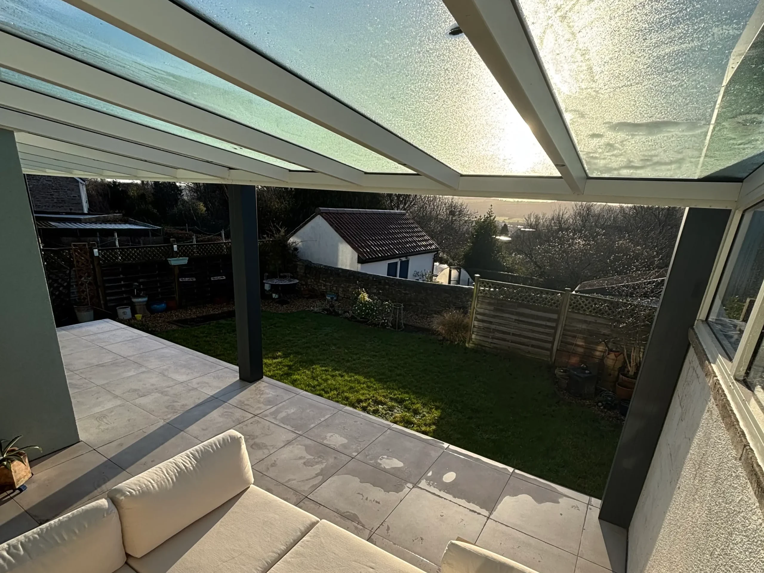 Cream garden sofa under an off white and anthracite grey aluminium framed glass roof veranda with LED spot lights.